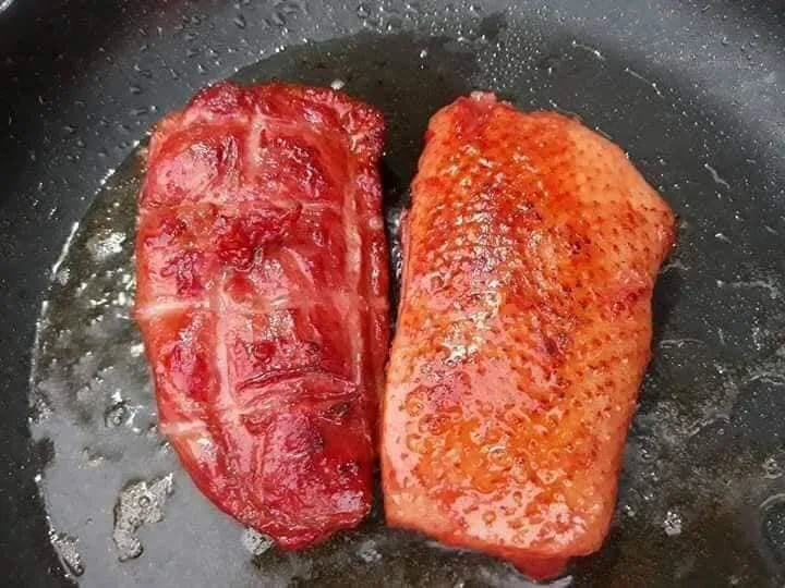 Hai miếng lườn ngỗng hun khói đang áp chảo, mỡ ngỗng chảy ra lòng chảo